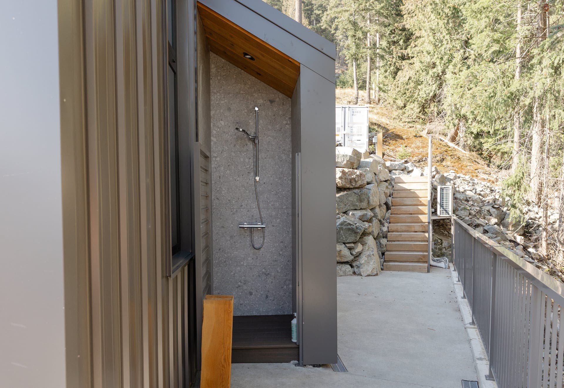 Open-sky outdoor shower with cedar wall and forest backdrop